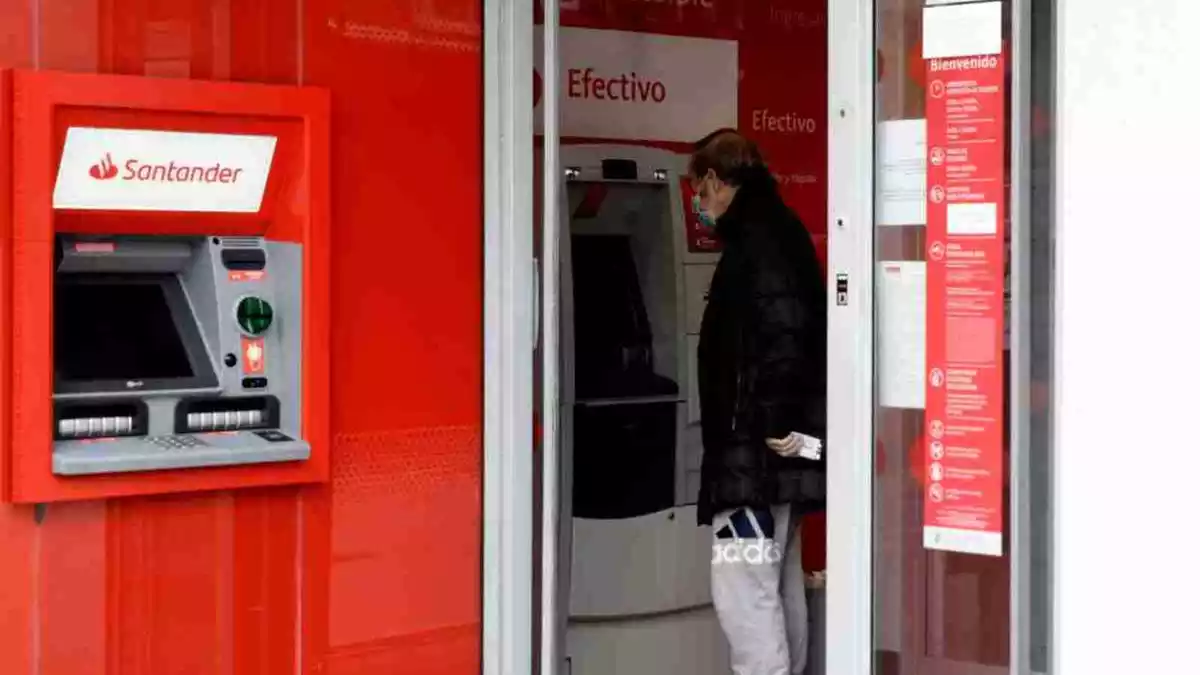 Una oficina del Banc Santander amb el caixer en primer pla i un client operant en un altre