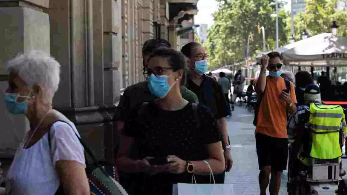Gent amb mascareta fent cua per entrar a una biblioteca de Barcelona