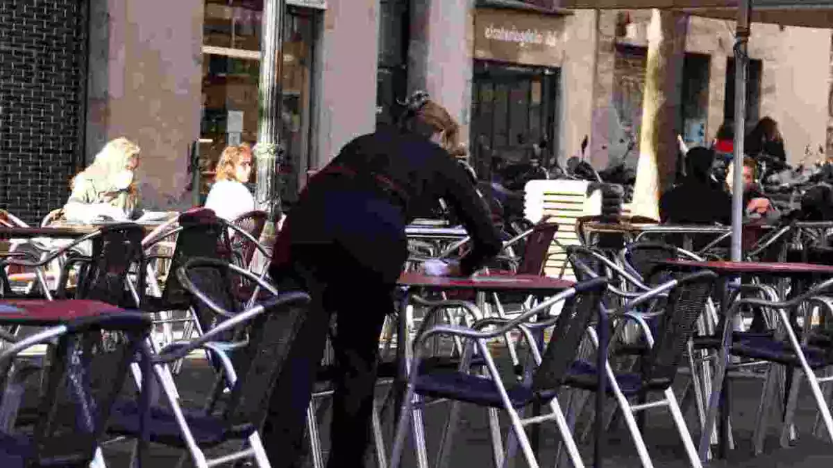 Pla mitjà d'una cambrera netejant una taula d'una terrassa del bar Las Euras a la plaça de la Vila de Gràcia