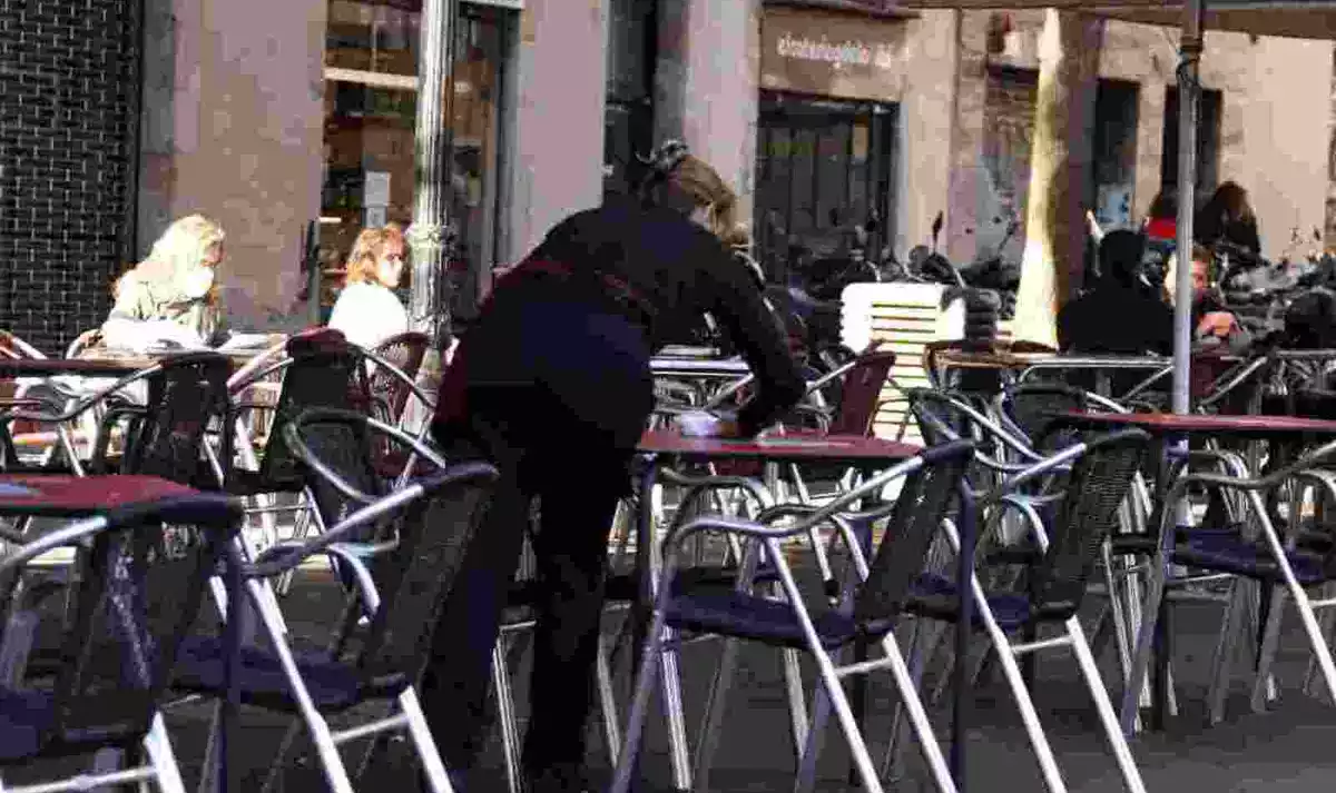 Pla mitjà d'una cambrera netejant una taula d'una terrassa del bar Las Euras a la plaça de la Vila de Gràcia