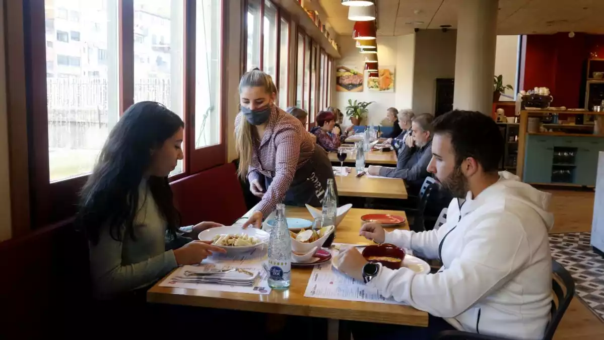 Una cambrera atenent una taula amb dos comensals en un restaurant de Girona