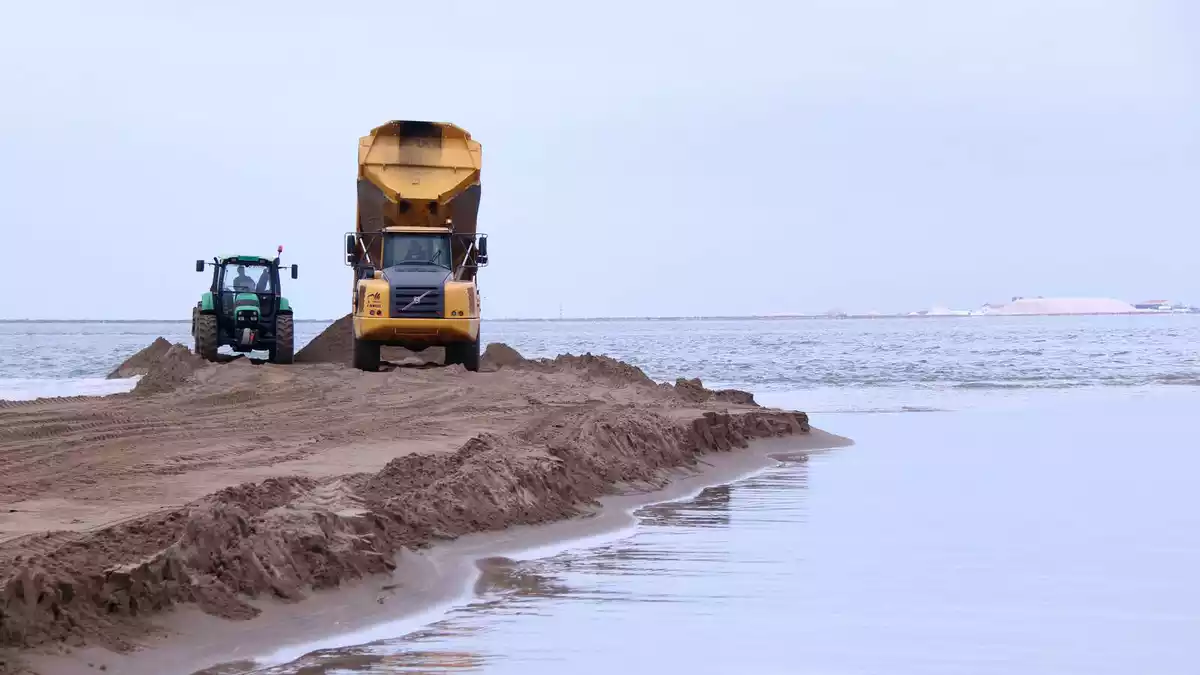 Pla general d'un camió abocant sorra al mar a la barra del Trabucador, amb les salines de la punta de la Bany al fons a la dreta.