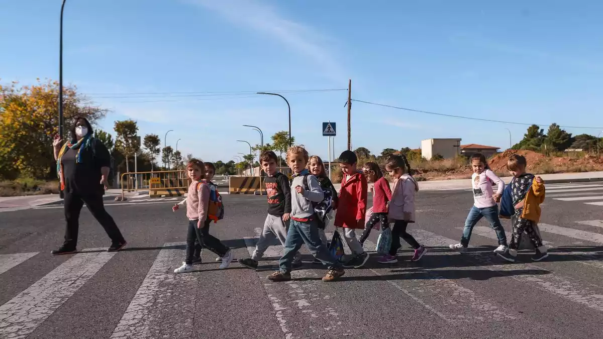 Un grup de nens acompanyats d'una mestra creuant un carrer per un pas zebra