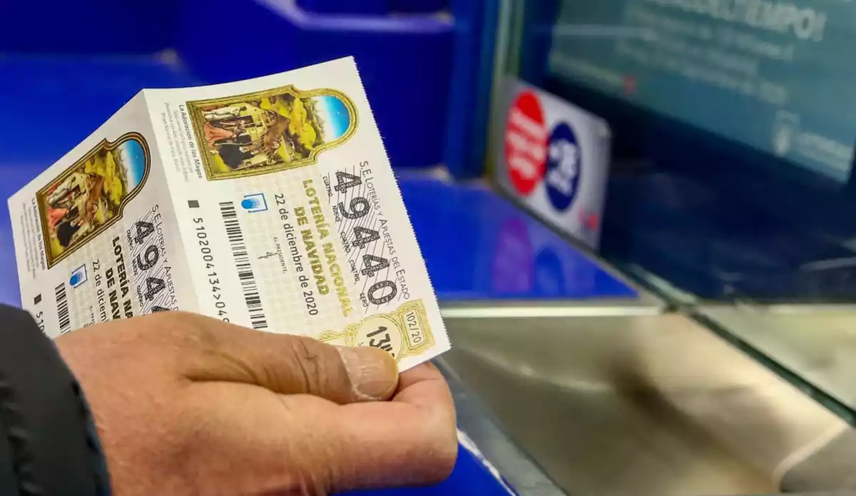 Imatge de dos dècims de la Loteria de Nadal, sostinguts per la mà d'un home en una administració