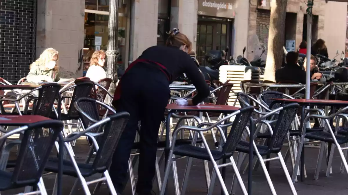 Pla mitjà d'una cambrera netejant una taula d'una terrassa del bar Las Euras a la plaça de la Vila de Gràcia