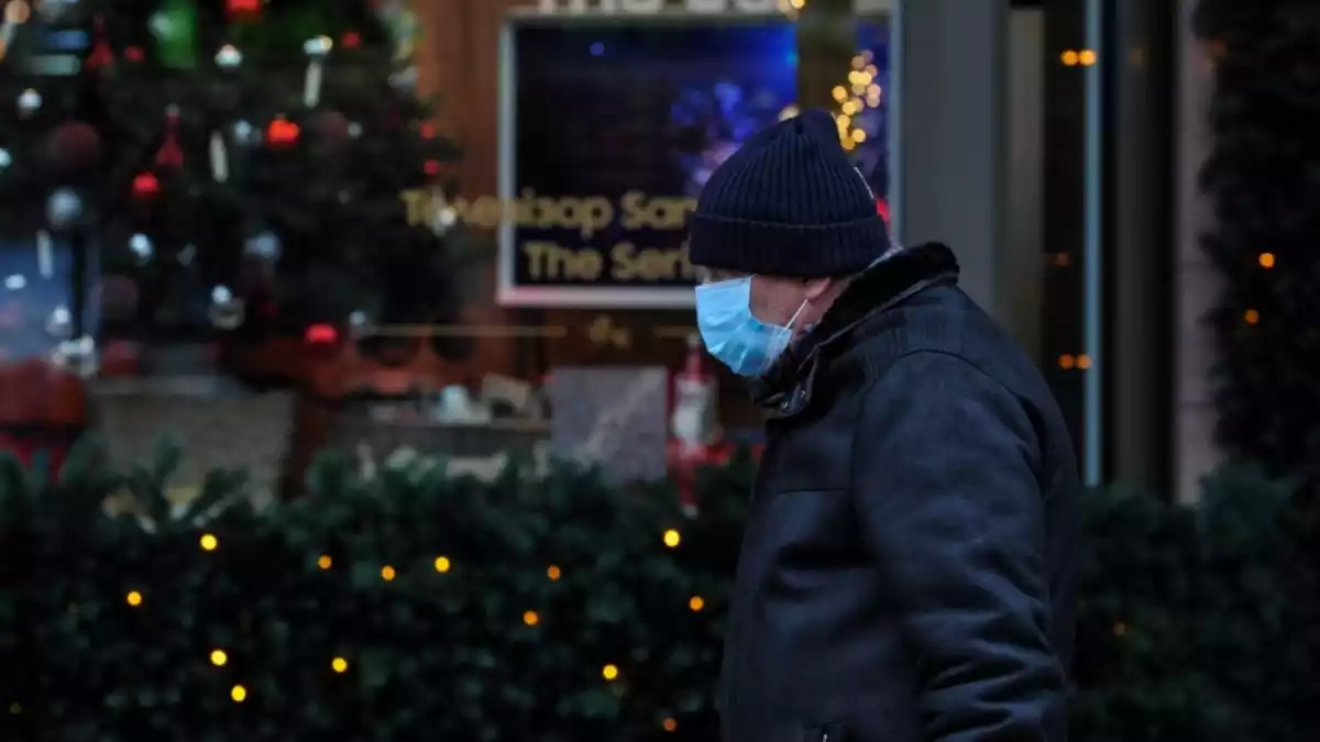 Un home amb mascareta passant per davant d'un arbre de Nadal i decoració diversa