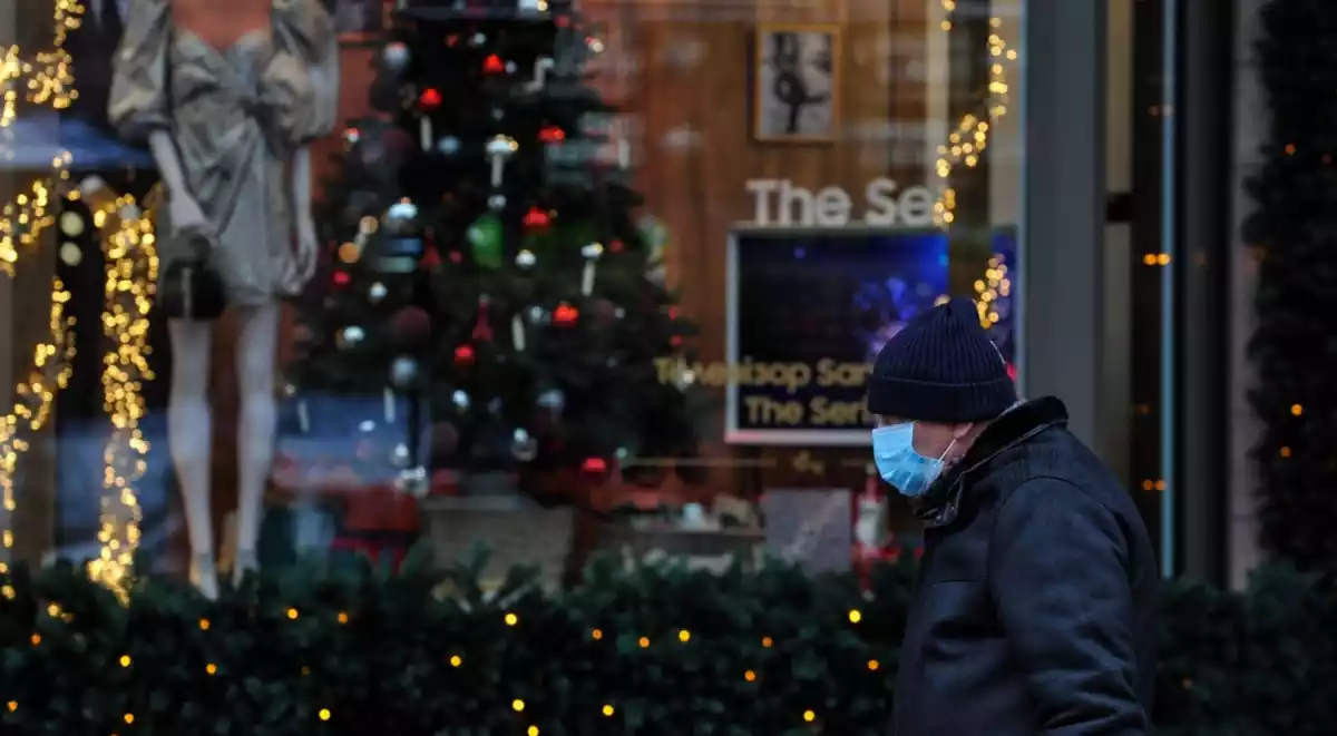 Un home amb mascareta passant per davant d'un arbre de Nadal i decoració diversa