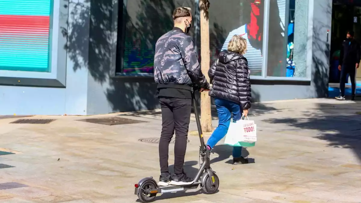 Imatge d'una persona sobre un patinet elèctric en un carrer per a vianants de la ciutat de Madrid