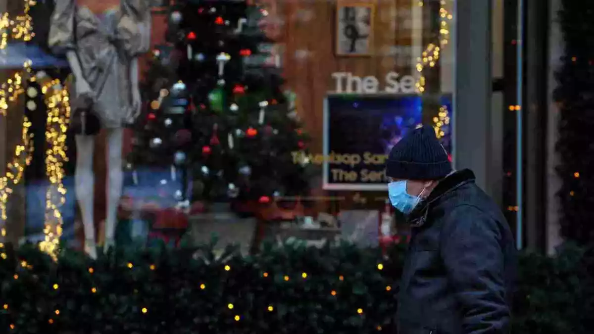 Un home amb mascareta passant per davant d'un arbre de Nadal i decoració diversa