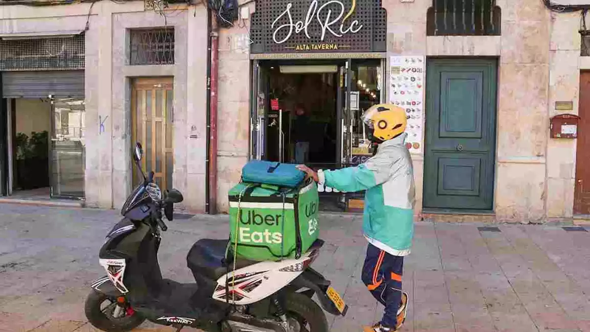 Pla general d'un repartidor a domicili esperant la comanda d'un restaurant de la plaça de la Font en el primer dia de restriccions