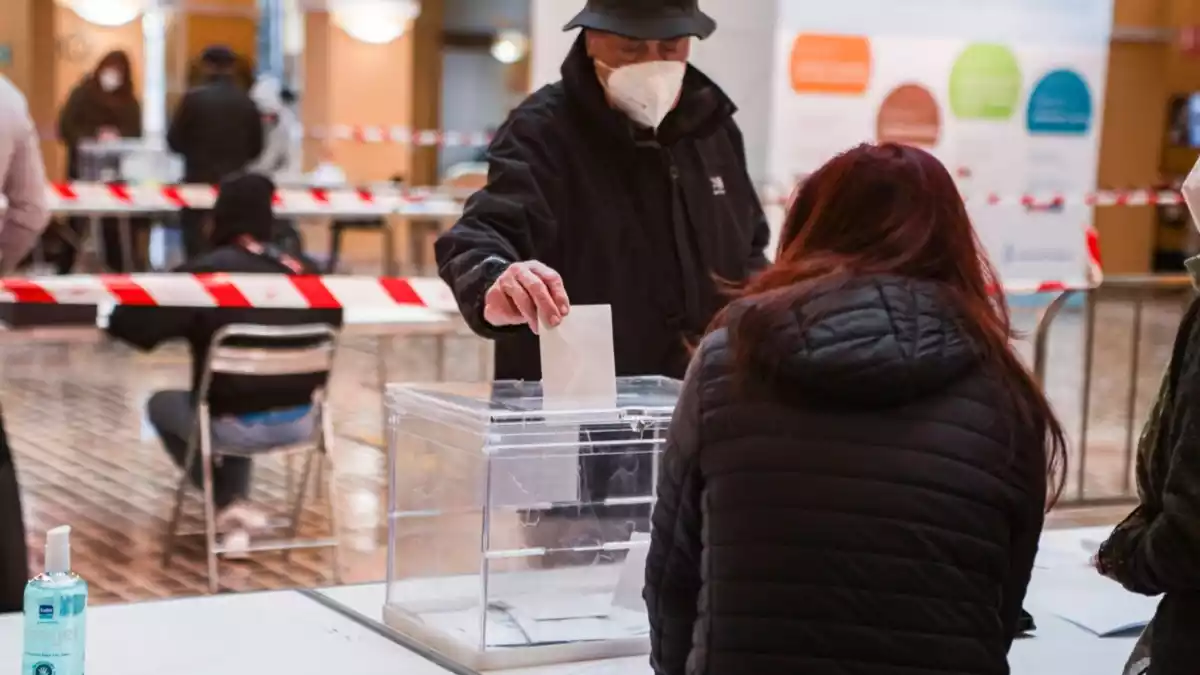 Un home, amb barret i mascareta, diposita el seu vot en una urna
