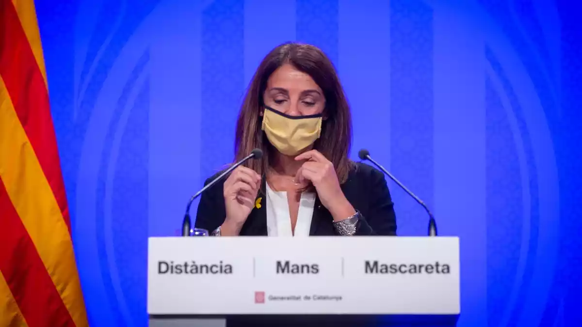 La portaveu del Govern, Meritxell Budó, en roda de premsa amb fons blau i mascareta