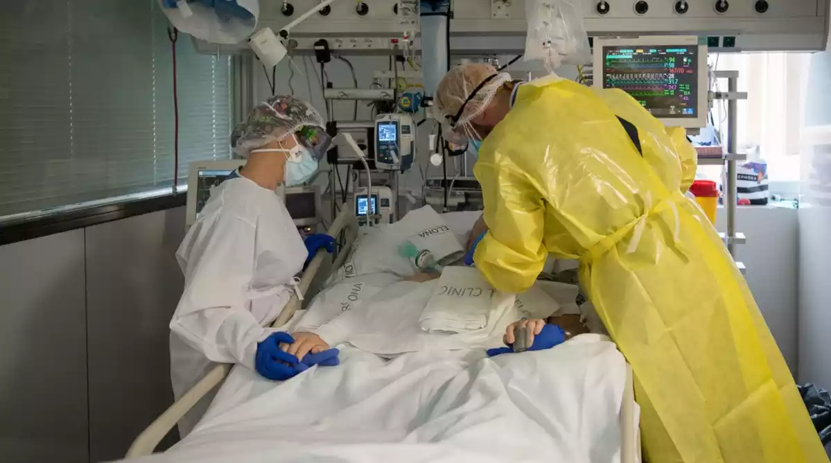Pla mitjà de dos sanitaris visitant un pacient de Covid-19 a l'UCI de l'Hospital Clínic protegits amb EPI