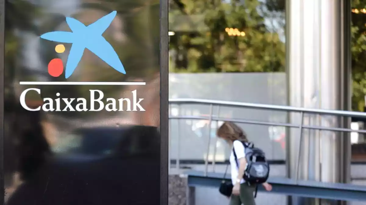 El logo de CaixaBank amb una persona passant per darrere de dia