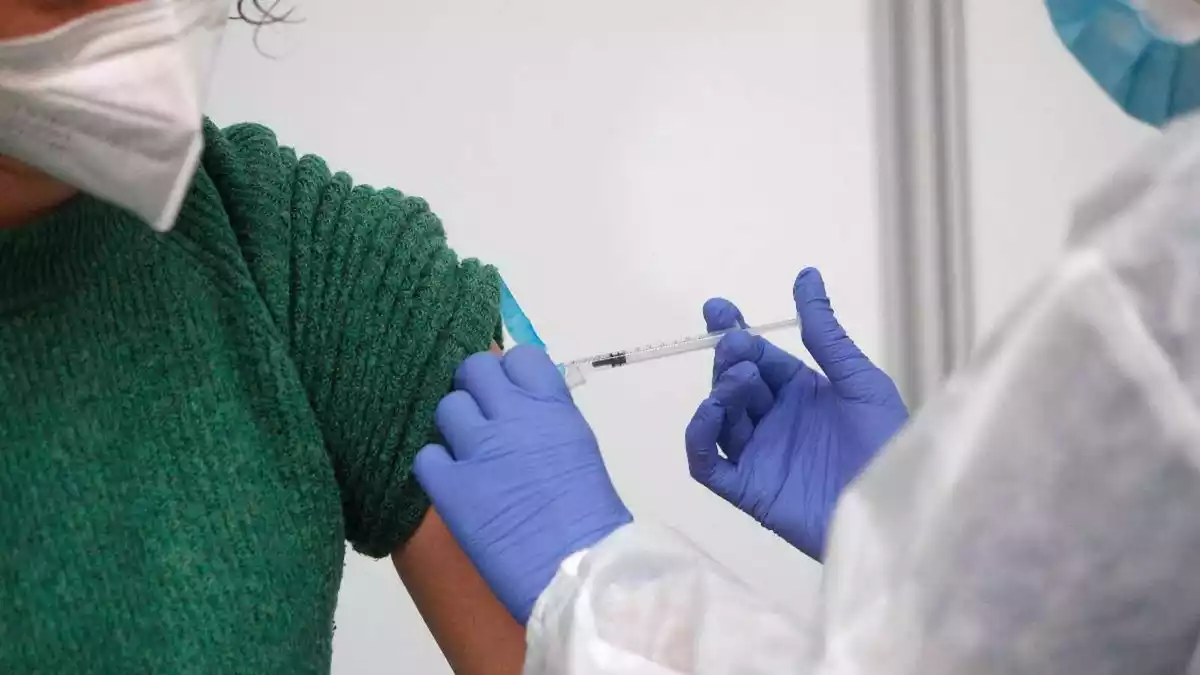Una sanitària administra una dosi de la vacuna contra la Covid-19 a una dona amb mascareta
