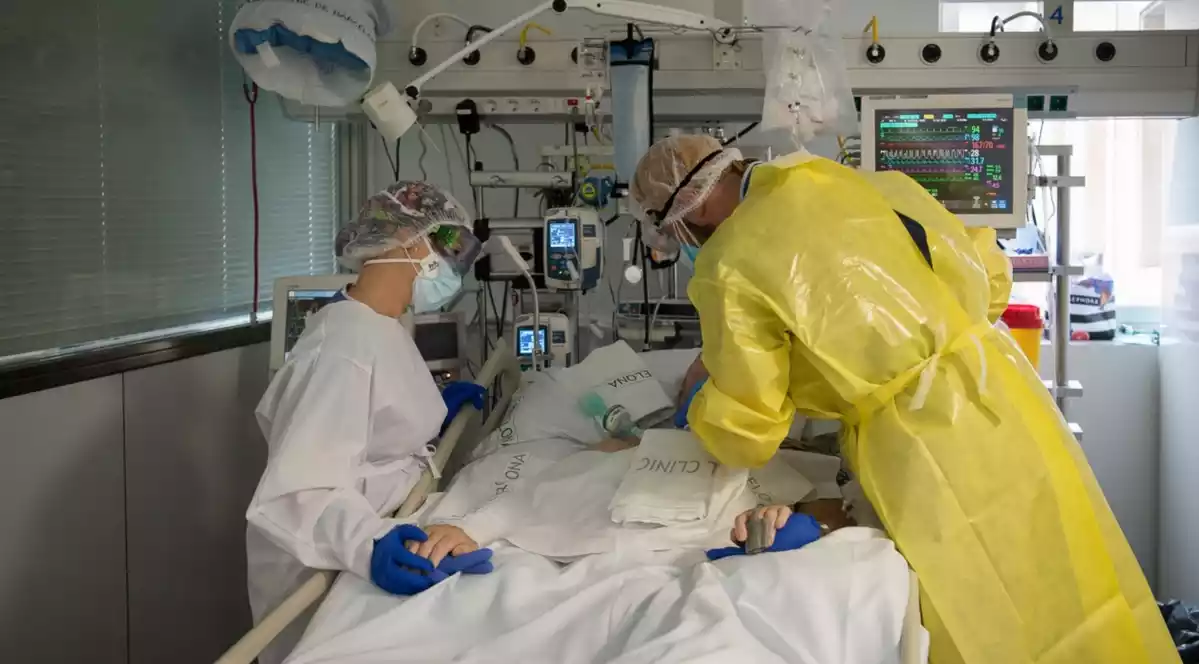 Pla mitjà de dos sanitaris visitant un pacient de Covid-19 a l'UCI de l'Hospital Clínic protegits amb EPI