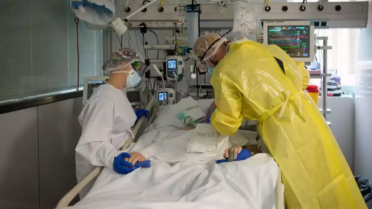 Pla mitjà de dos sanitaris visitant un pacient de Covid-19 a l'UCI de l'Hospital Clínic protegits amb EPI