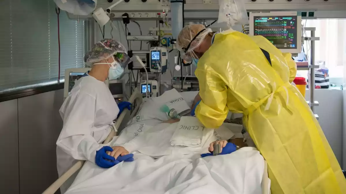 Pla mitjà de dos sanitaris visitant un pacient de Covid-19 a l'UCI de l'Hospital Clínic protegits amb EPI