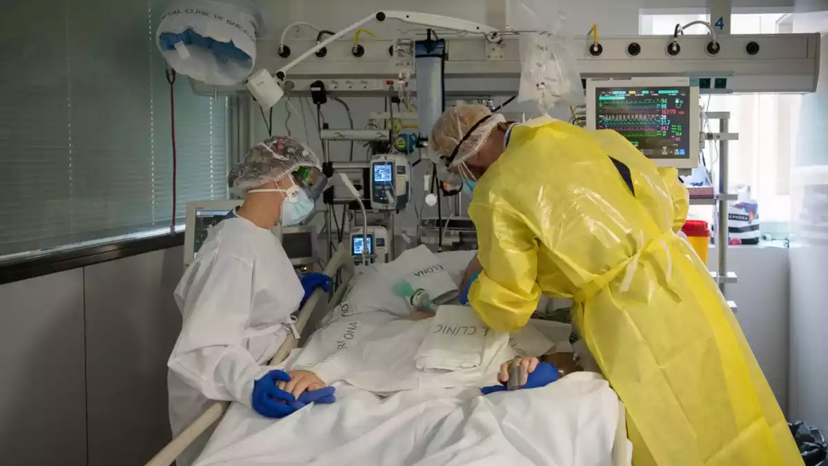 Pla mitjà de dos sanitaris visitant un pacient de Covid-19 a l'UCI de l'Hospital Clínic protegits amb EPI