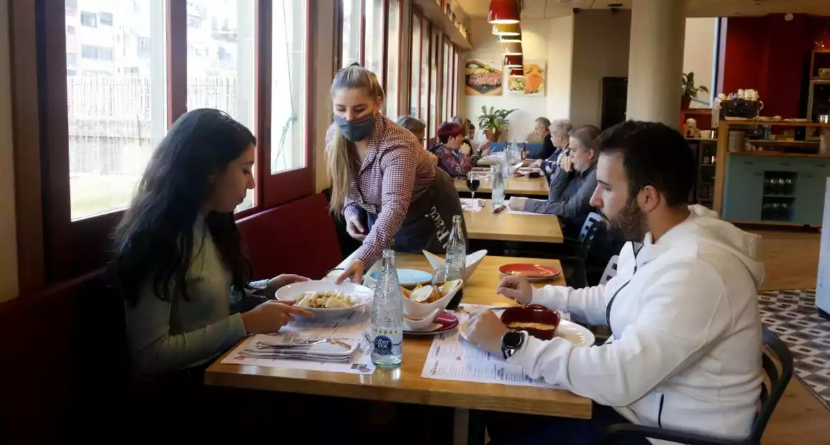 Una cambrera atenent una taula amb dos comensals en un restaurant de Girona