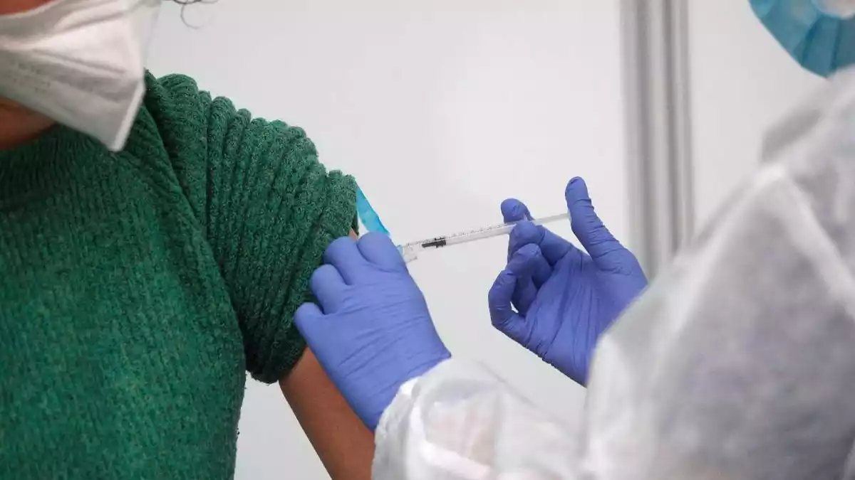 Una sanitària administra una dosi de la vacuna contra la Covid-19 a una dona amb mascareta
