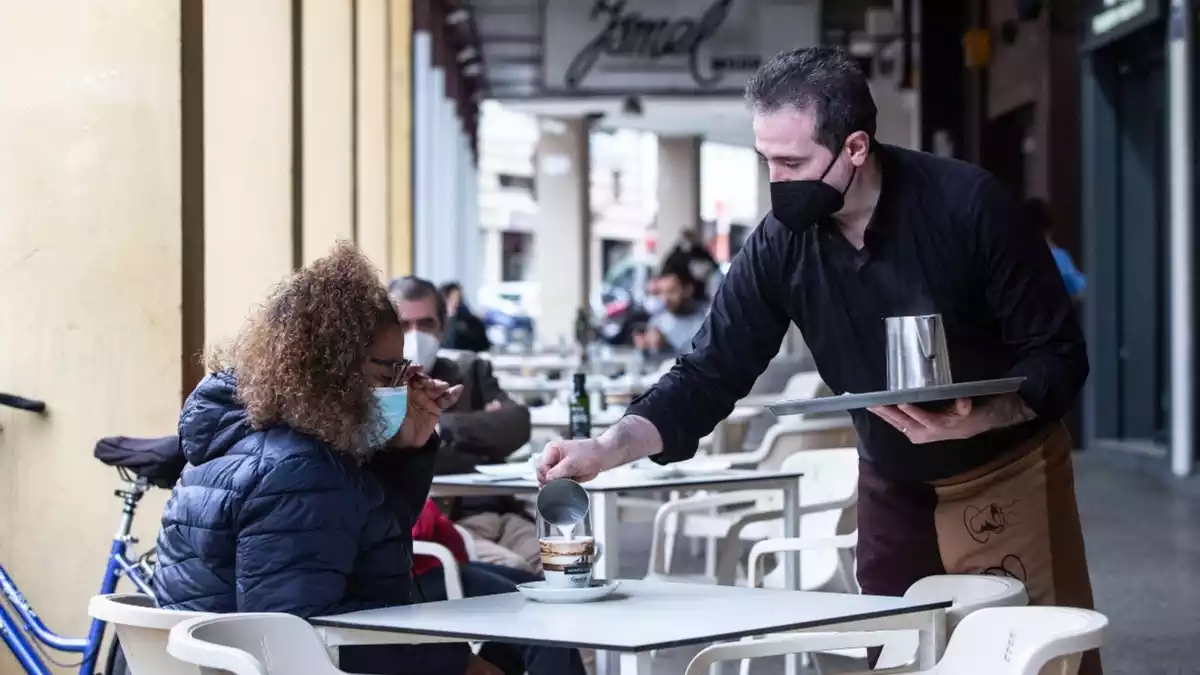 Imatge d'un cambrer servint un cafè a una clienta en una terrassa