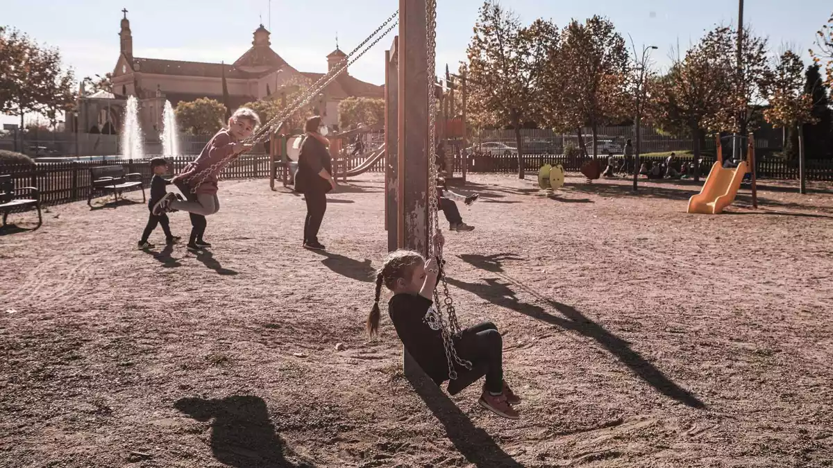 Dues nenes als gronxadors d'un parc infantil, amb el Santuari de Misericòrdia de Reus al fons