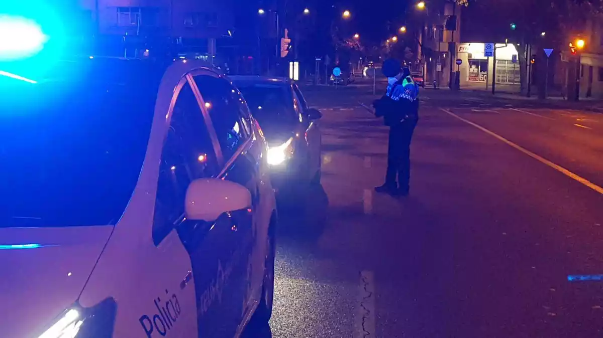 En primer pla, un cotxe de la Guàrdia Urbana de Reus; al darrere un cotxe particular i, al costat, un agent posant una multa