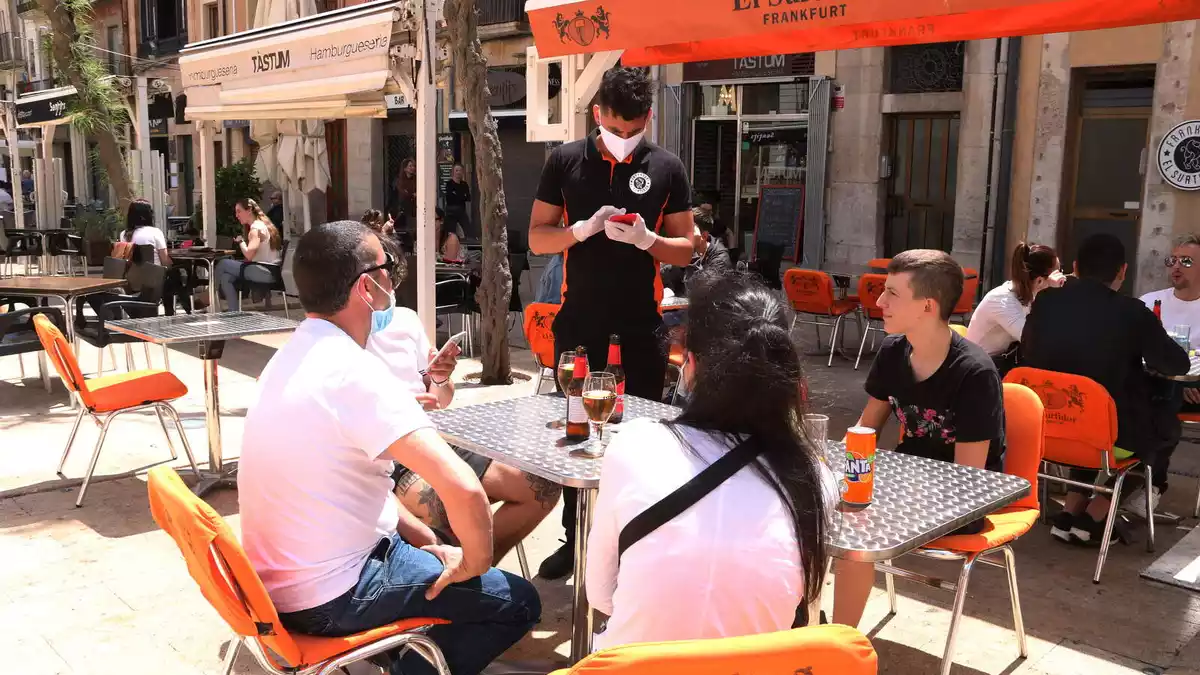Pla obert d'un cambrer anotant la comada a uns clients en una terrassa de la plaça de la Font de Tarragona en el primer dissabte de la fase 1.