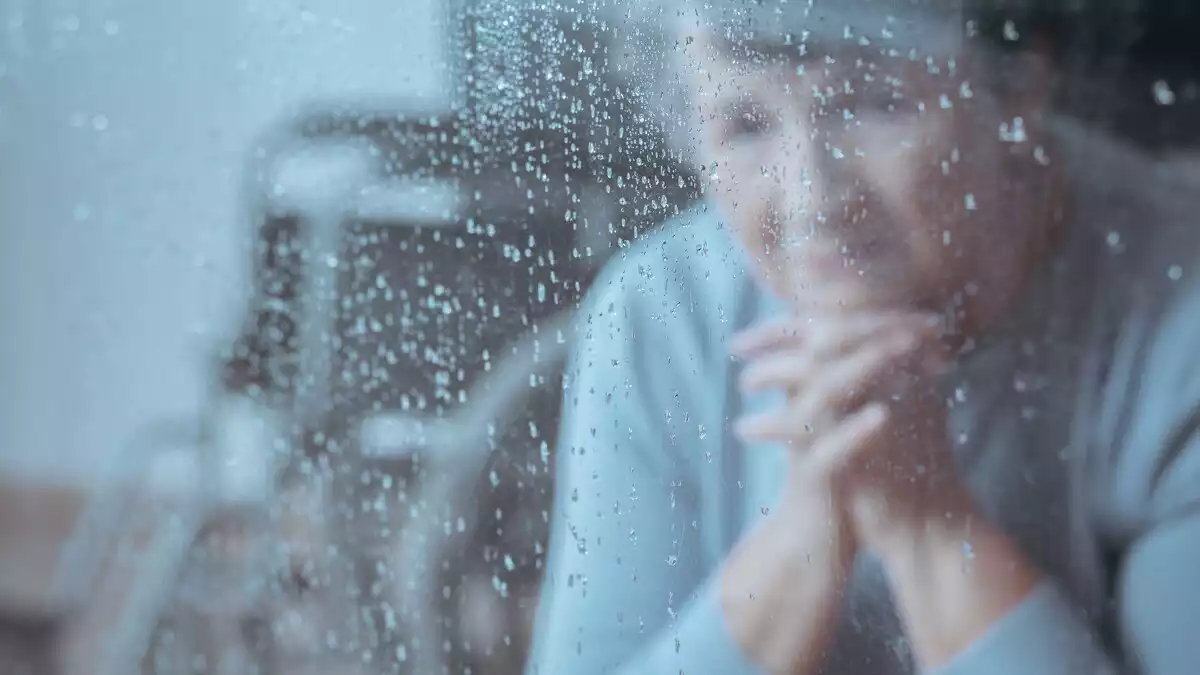 Imagen de una mujer mirando por la ventana con posado triste