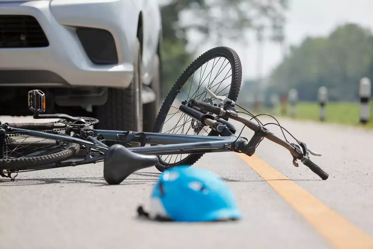 Una bicicleta tendida en el suelo junto a un casco azul y delante de un vehículo
