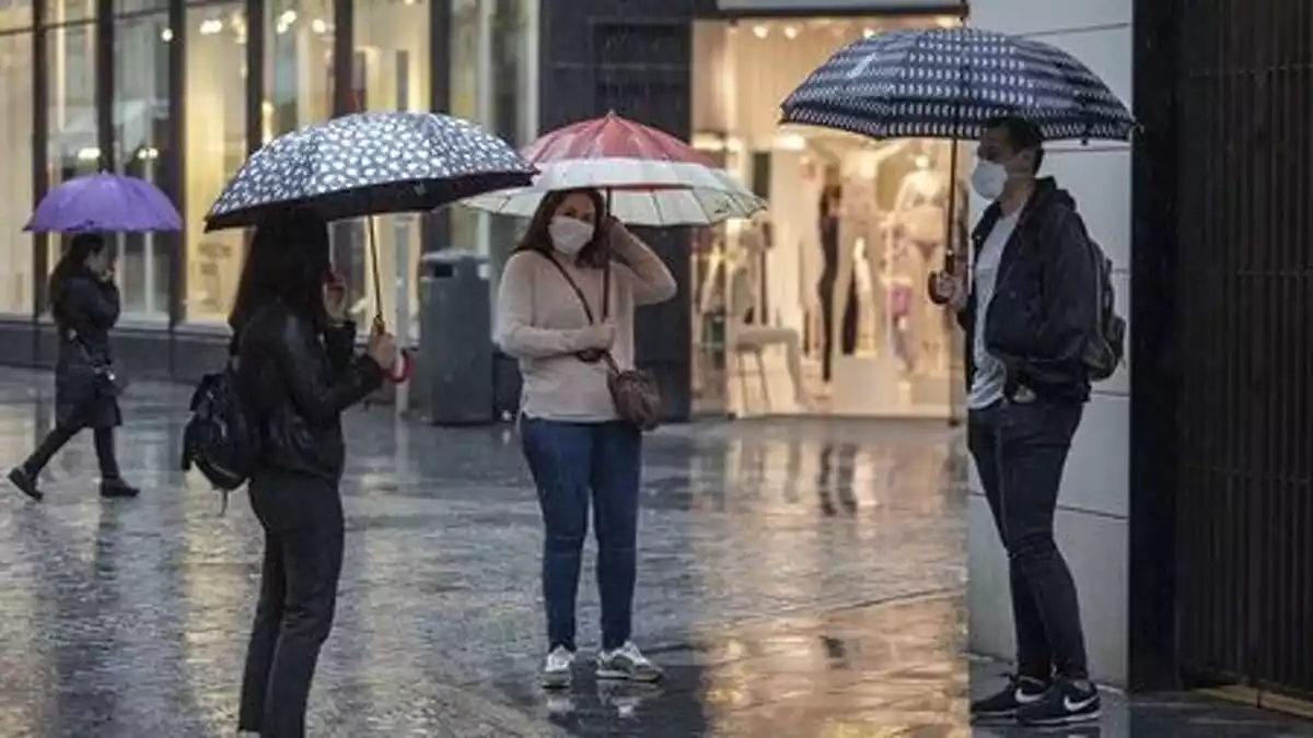Varias personas conversan bajo la lluvia protegidos con sus paraguas