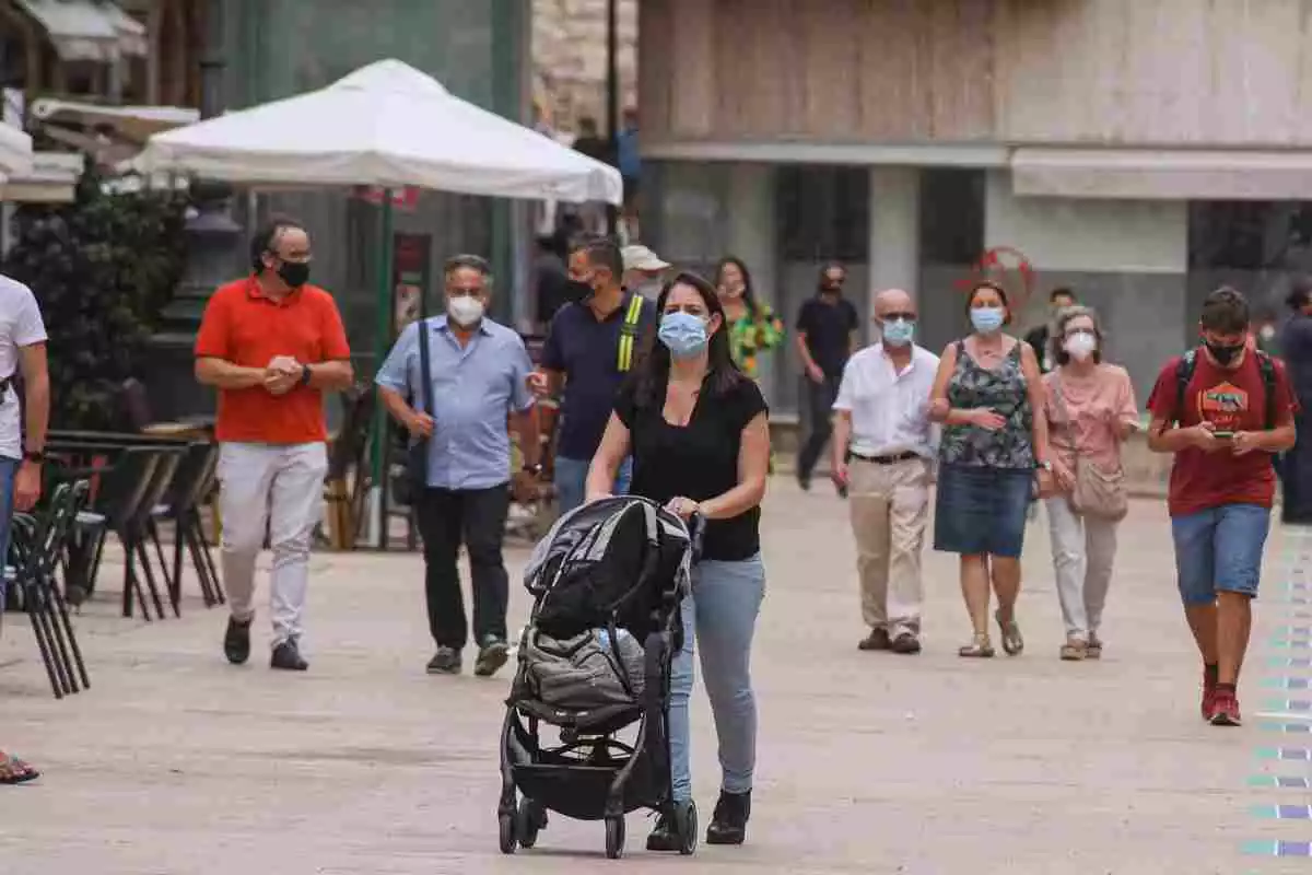Un grupo de gente con una mujer empujando un carrito en primer plano paseando por la calle durante la pandemia