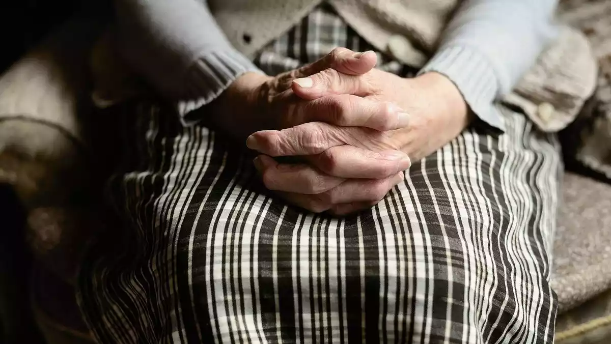 Imagen de archivo de una mujer de edad avanzada sentada y con las manos cruzadas
