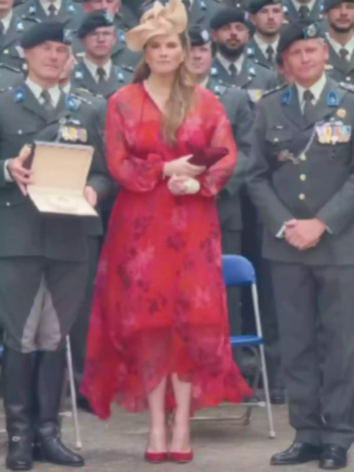 Dona amb vestit vermell i barret elegant posant al costat de dos homes uniformats en un acte oficial Dona amb vestit vermell i barret elegant posant al costat de dos homes uniformats en un acte oficial