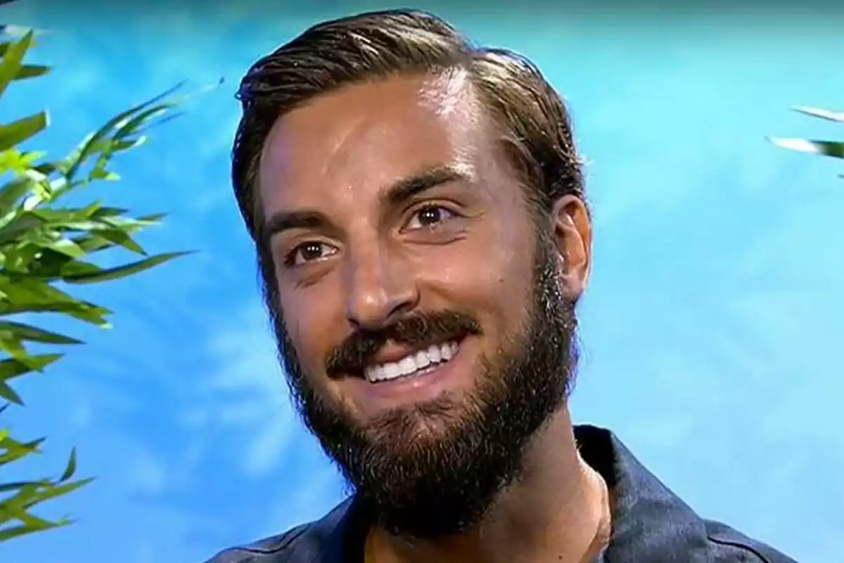 Borja González, un jove amb barba i cabell curt, somriu davant d’un fons blau amb plantes als costats a Supervivientes. Borja González, un jove amb barba i cabell curt, somriu davant d’un fons blau amb plantes als costats a Supervivientes.