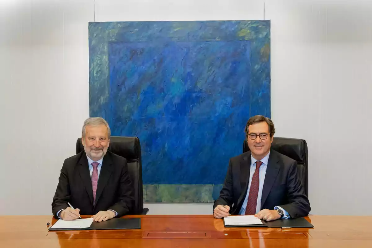 Dos homes amb vestit i corbata asseguts en una taula de fusta signant documents amb una pintura abstracta blava de fons Dos homes amb vestit i corbata asseguts en una taula de fusta signant documents amb una pintura abstracta blava de fons