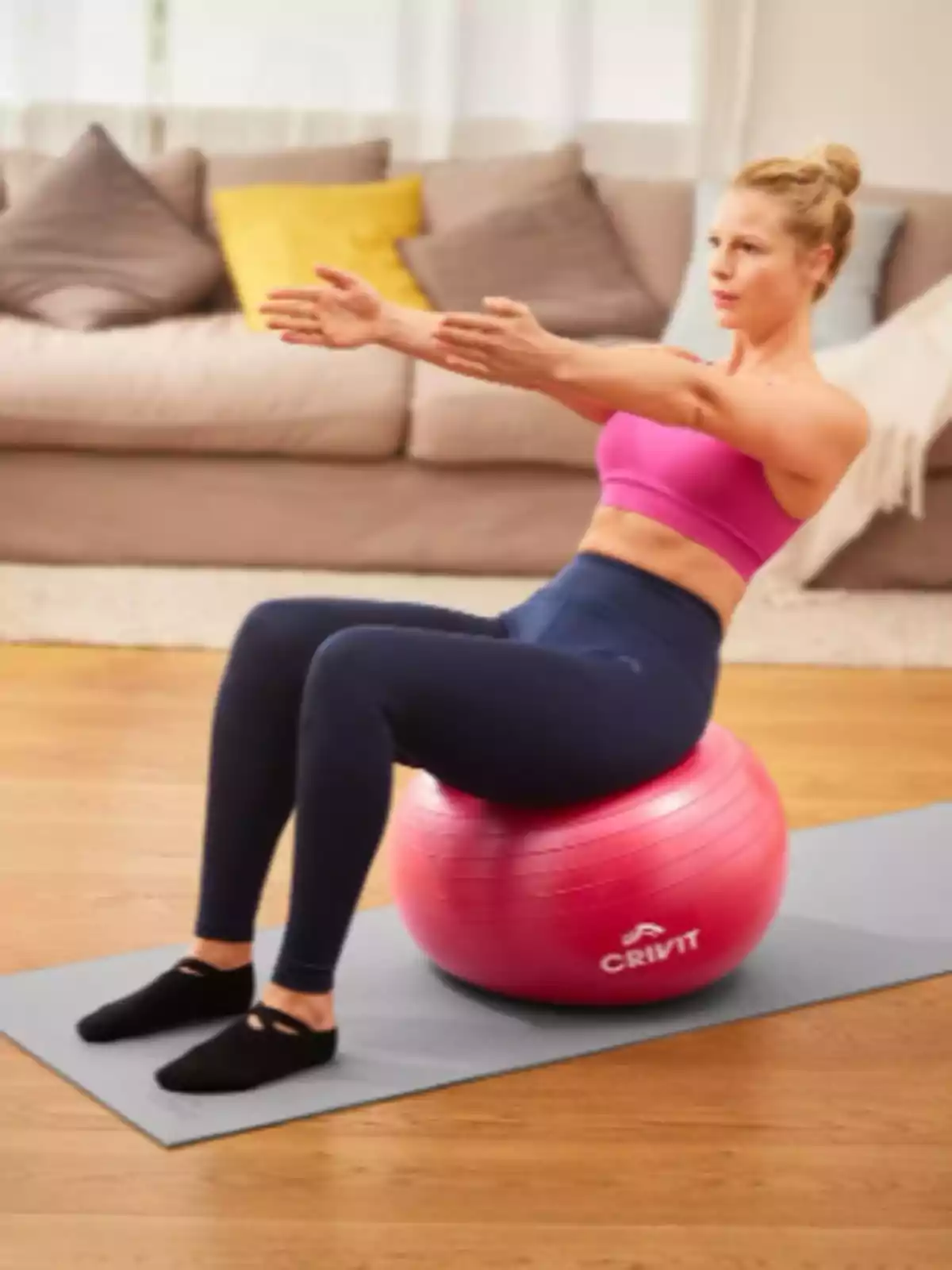 Dona fent exercici asseguda sobre una pilota de pilates rosa en una sala d’estar Dona fent exercici asseguda sobre una pilota de pilates rosa en una sala d’estar