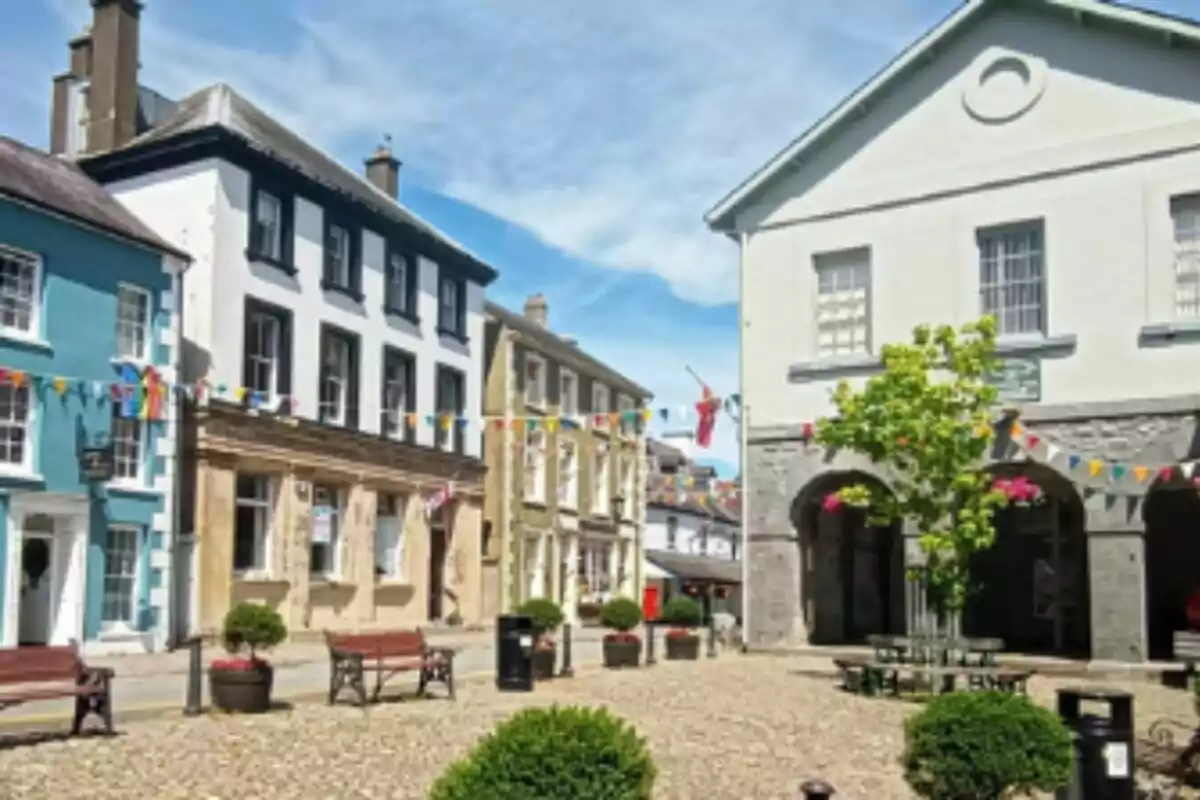 Plaza pintoresca con bancos de madera, edificios coloridos y banderines decorativos bajo un cielo azul en Carmarthenshire. Plaza pintoresca con bancos de madera, edificios coloridos y banderines decorativos bajo un cielo azul en Carmarthenshire.