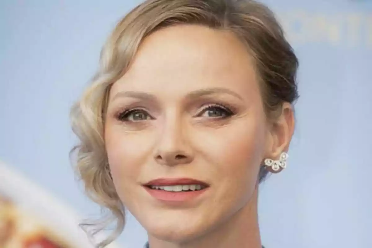 Primer plano de Charlene de Mónaco con maquillaje suave y aretes brillantes, fondo azul desenfocado. Primer plano de Charlene de Mónaco con maquillaje suave y aretes brillantes, fondo azul desenfocado.