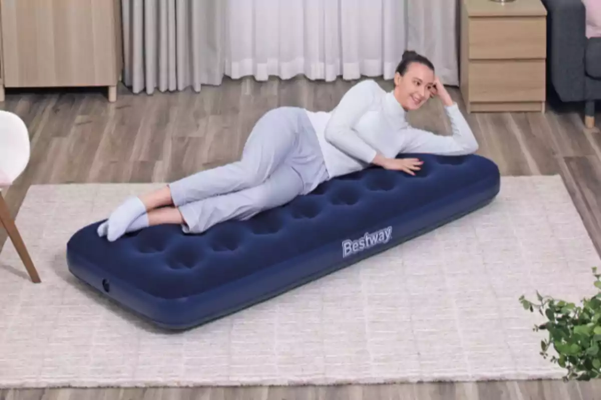 Dona estirada sobre un matalàs inflable blau en una habitació amb terra de fusta i catifa clara Dona estirada sobre un matalàs inflable blau en una habitació amb terra de fusta i catifa clara