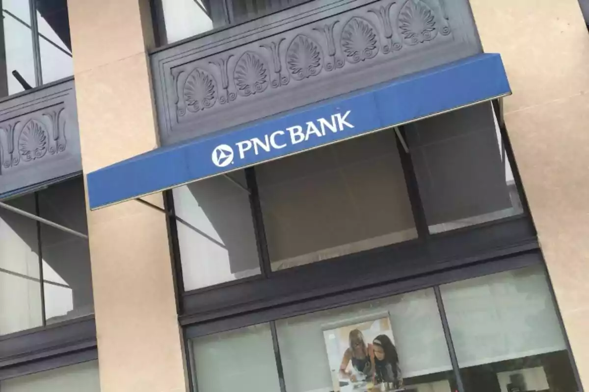 Façana d’un banc PNC amb tendal blau i finestres grans.