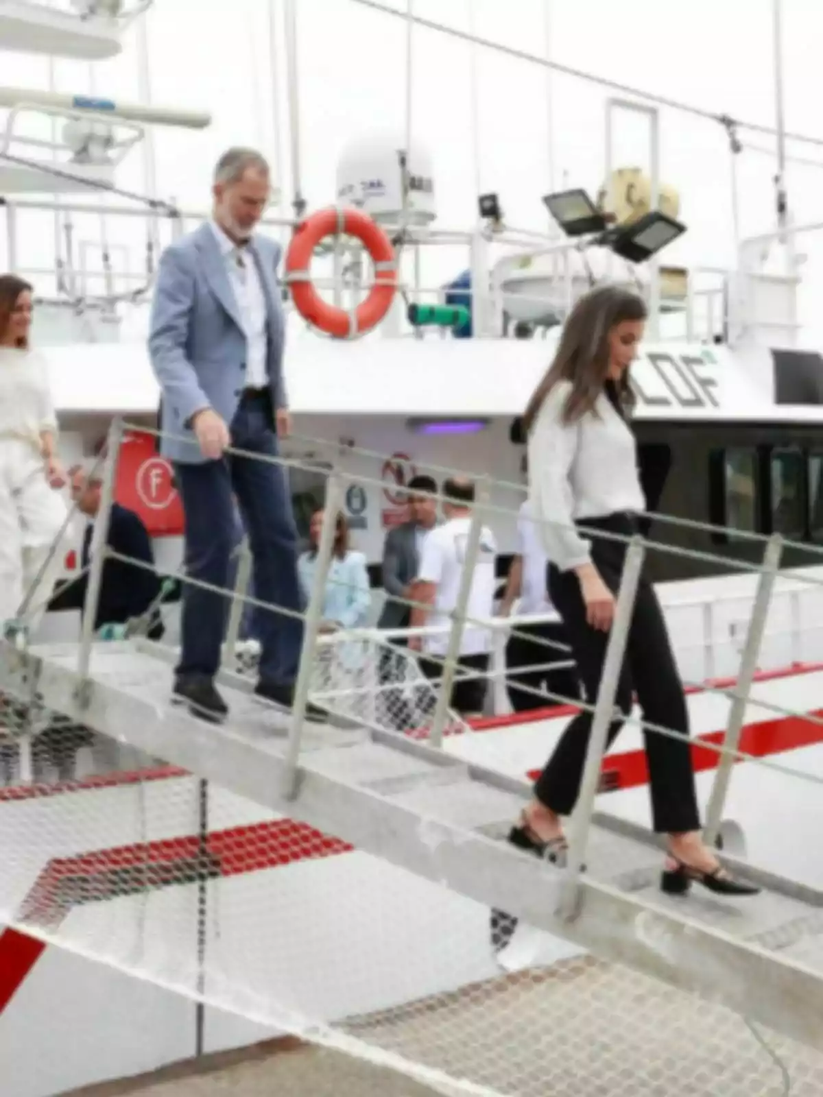 Felipe and Letizia going down a metal gangway from a white boat with red details. Felipe and Letizia going down a metal gangway from a white boat with red details.