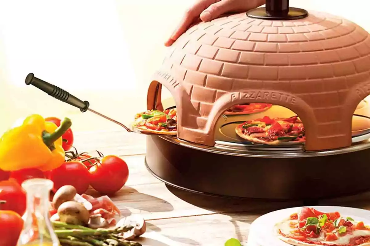 Horno de mesa en forma de iglú cocinando mini pizzas con ingredientes frescos como pimientos, tomates, champiñones y espárragos alrededor Horno de mesa en forma de iglú cocinando mini pizzas con ingredientes frescos como pimientos, tomates, champiñones y espárragos alrededor