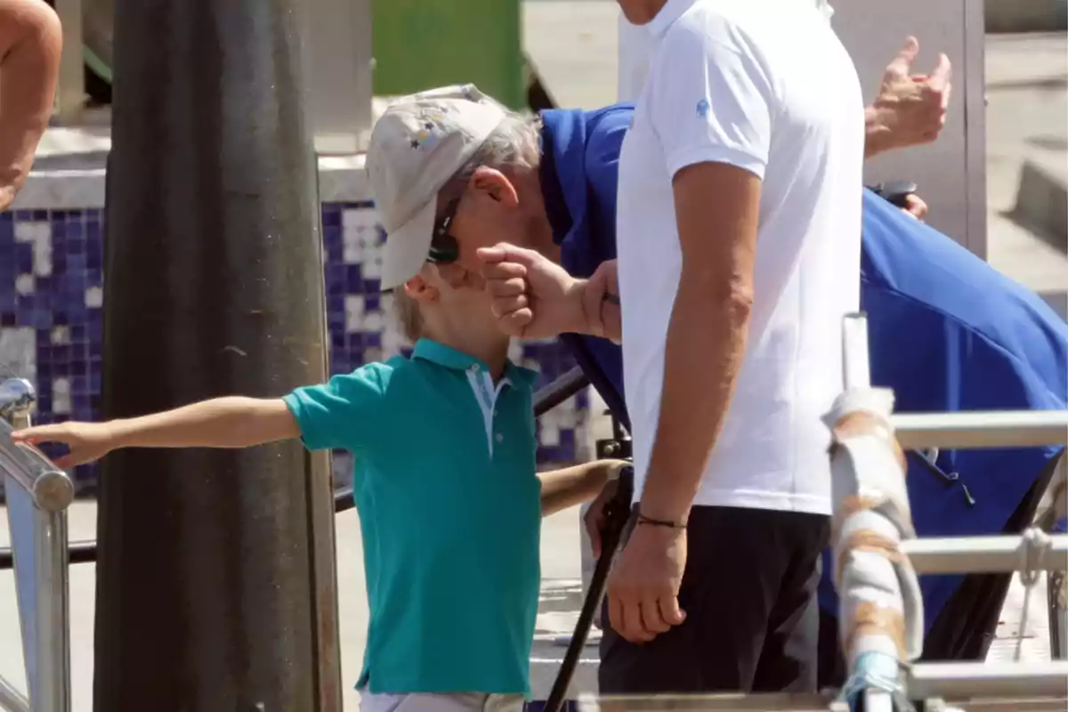 Carlitos Zurita amb samarreta verda i gorra és acompanyat per dos adults, un d'ells és el rei Joan Carles I, a prop d’una barana en un entorn a l’aire lliure. Carlitos Zurita amb samarreta verda i gorra és acompanyat per dos adults, un d'ells és el rei Joan Carles I, a prop d’una barana en un entorn a l’aire lliure.