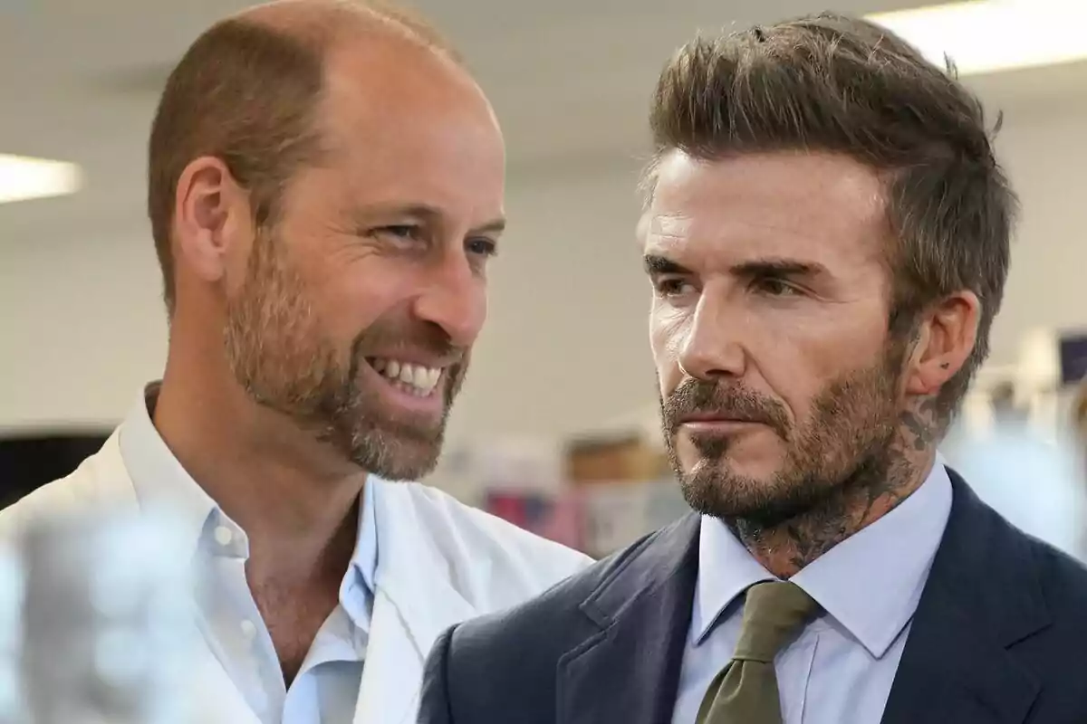 Two middle-aged men are talking indoors; one of them is smiling while the other looks serious and is wearing a formal suit. Two middle-aged men are talking indoors; one of them is smiling while the other looks serious and is wearing a formal suit.
