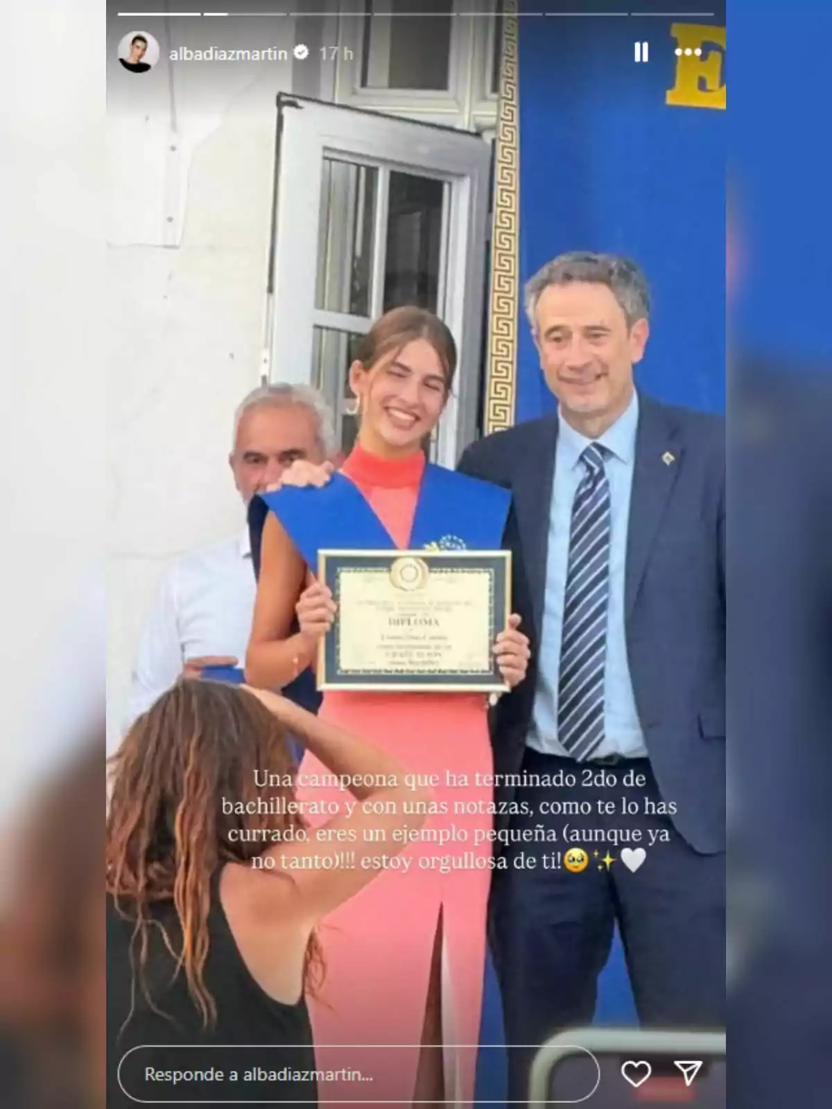Jove somrient amb una banda blava i un diploma a la mà posant al costat d’un home amb vestit durant una cerimònia de graduació. Jove somrient amb una banda blava i un diploma a la mà posant al costat d’un home amb vestit durant una cerimònia de graduació.