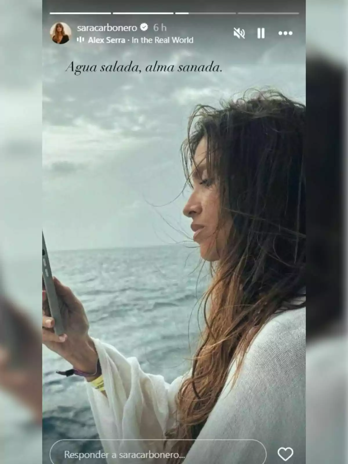 Sara Carbonero de perfil amb els cabells solts mirant el seu telèfon mòbil davant del mar en un dia ennuvolat.