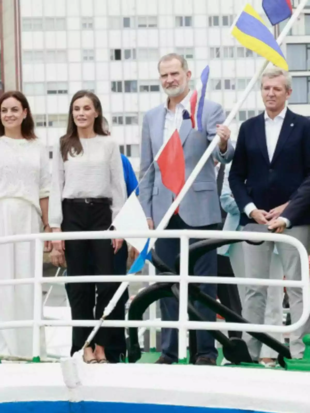 Four people—including Felipe and Letizia—pose on the deck of a boat next to several colorful flags and a building in the background. Four people—including Felipe and Letizia—pose on the deck of a boat next to several colorful flags and a building in the background.