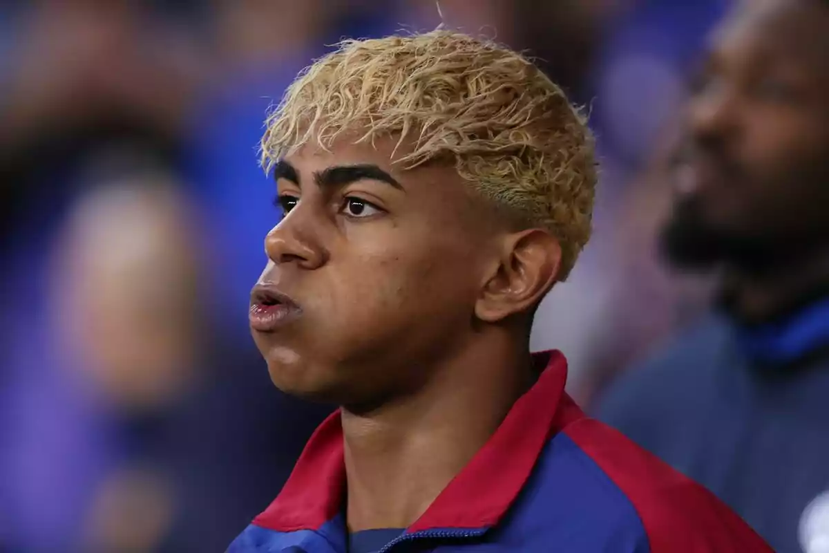 Young man with curly blond hair and a blue and red sports jacket looking straight ahead with a serious expression Young man with curly blond hair and a blue and red sports jacket looking straight ahead with a serious expression